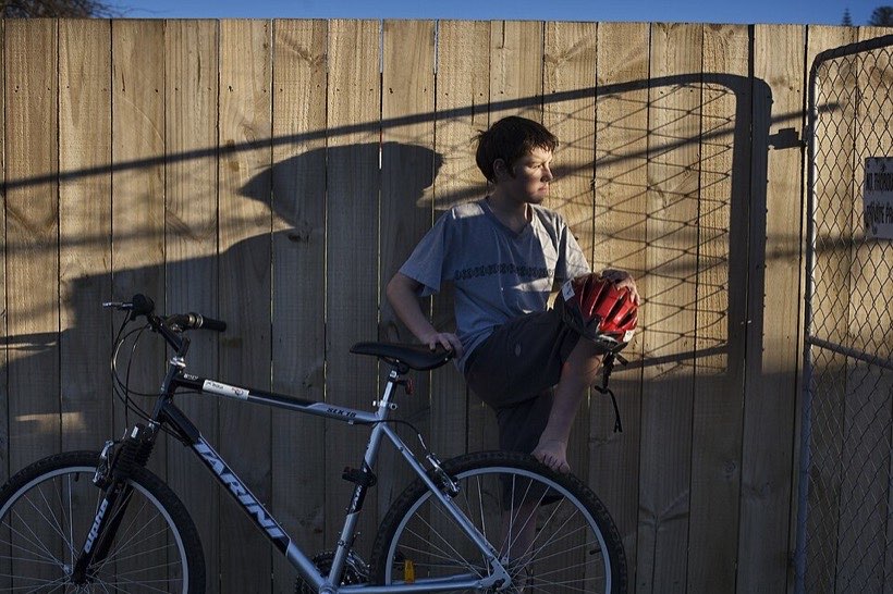 A boy and his bicycle make shadows on a fence.