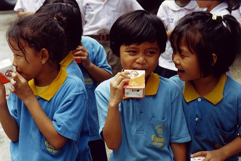 Children drinking milk from small cartons. Shops sell drinks in packs of 4 or 6.